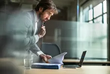 Worker comparing documents with computer data while sitting on a desk in the office.