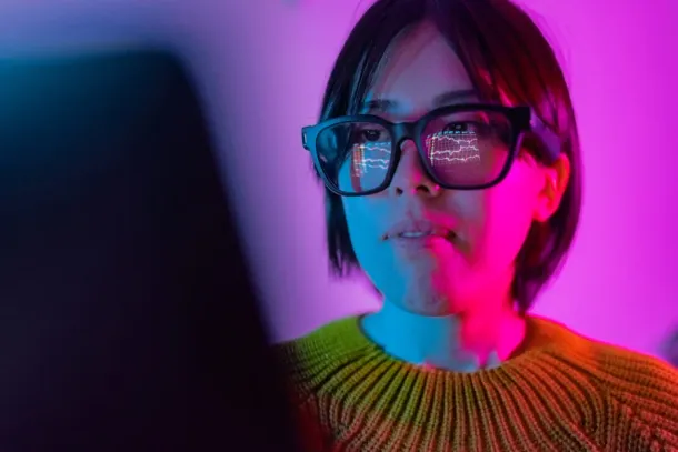 A woman is checking the chart for currency information on a laptop. The chart of cryptocurrency is reflected on smart glasses from laptop screen. Cryptocurrency concept.