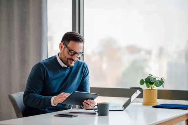 Young businessman using digital tablet while working on laptop in business office.