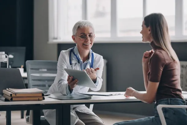 Confident female doctor pointing digital tablet while consulting patient in the medical office.