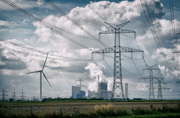 Brown-coal burning power plant with pollution, wind turbine and a group of electricity pylons.