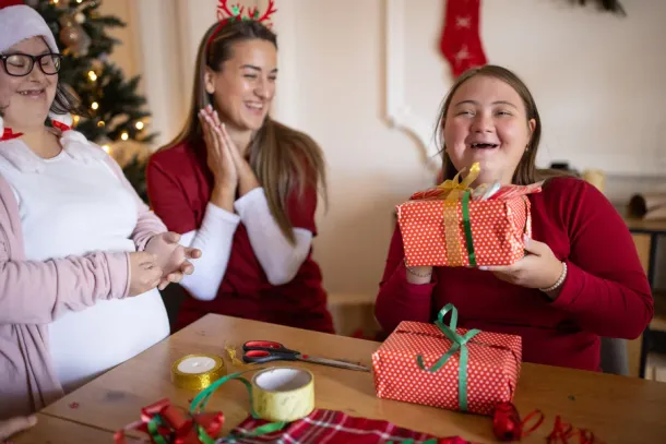 People with Down syndrome wrapping gifts together in the living room of a house with the help of their friends
