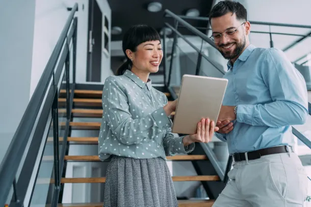 Shot of two colleagues using a digital tablet while walking down stairs in a modern office. Two business people in a motion on stairs in the office.