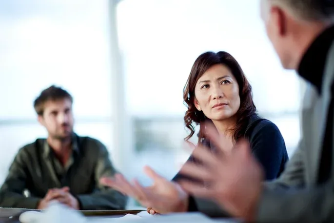 A women engaging in a serious meeting with two male colleagues.