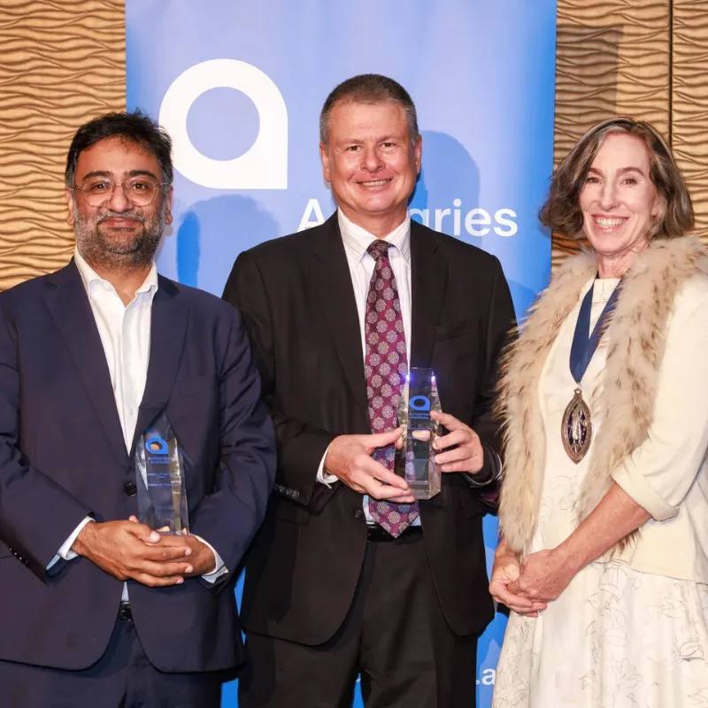Two men and a woman stand holding a trophy and smiling